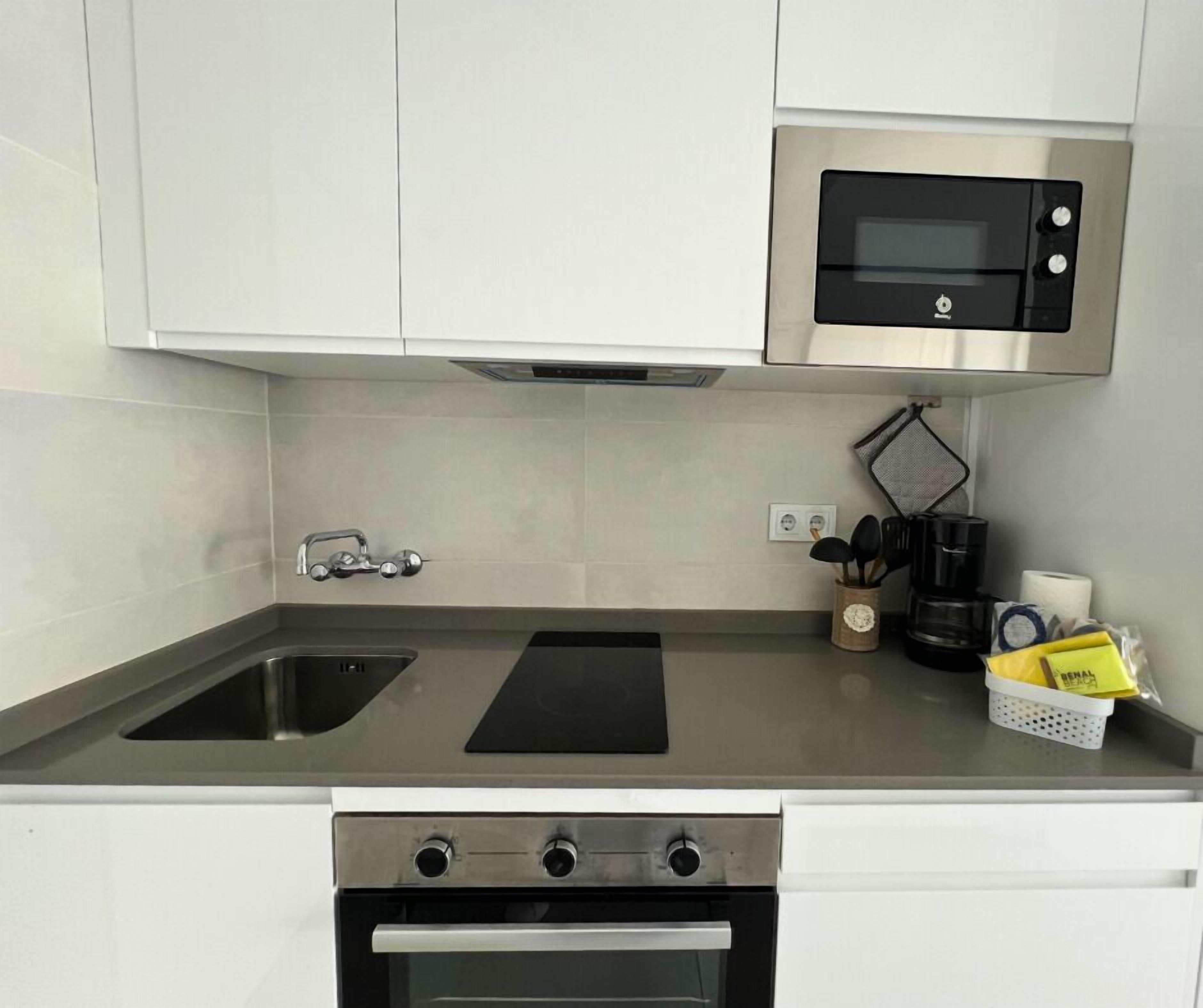 Een keuken met een rvs-spoelbak, een zwart inductiekookveld, een inbouwoven en een magnetron boven het kookveld.