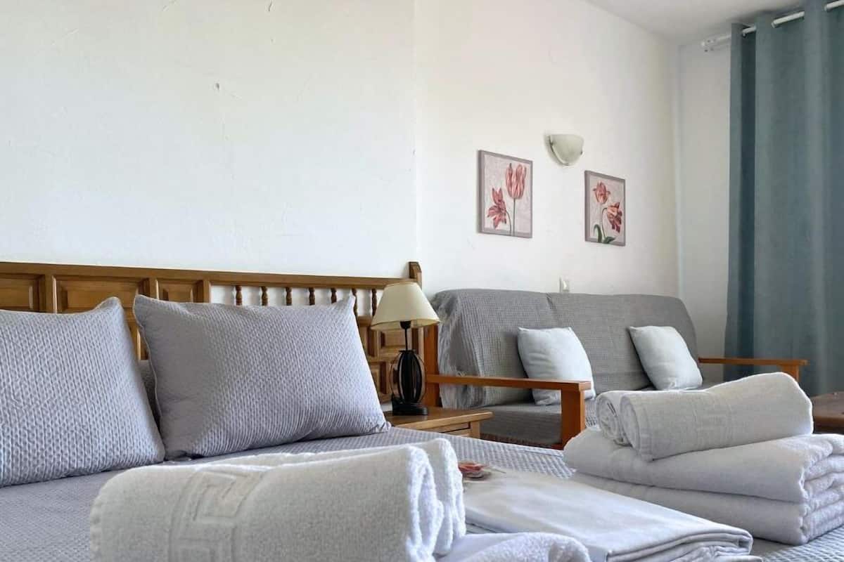 Une chambre d’hôtel avec un lit, un canapé et une table de chevet avec une lampe. Deux tableaux encadrés sont accrochés au mur.