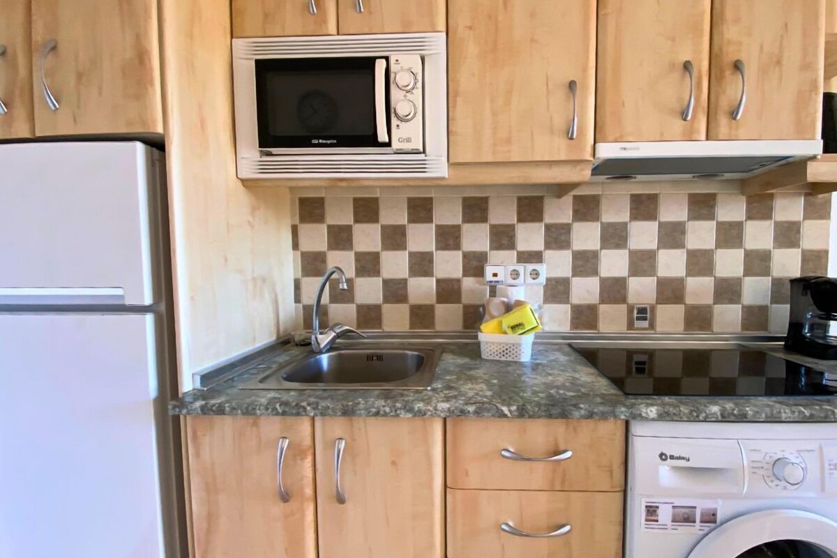 Une cuisine avec des meubles de rangement en bois, un four à micro-ondes, un évier et un lave-linge.