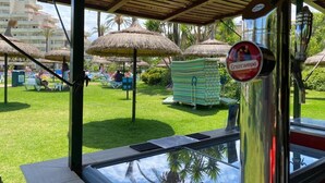 A beachside area with thatched umbrellas, a pool, and a sign for 'Cruzcampo'.