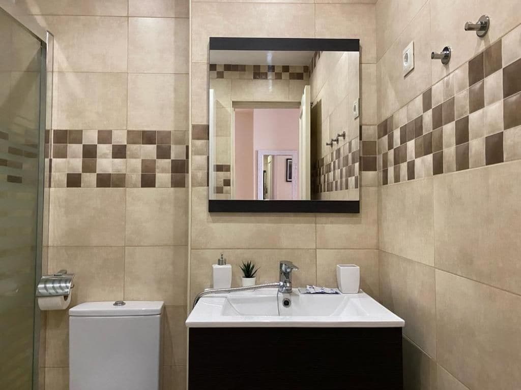 A bathroom with a toilet, sink, mirror, and tiled walls.