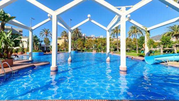 A swimming pool with white pillars and a clear blue sky.
