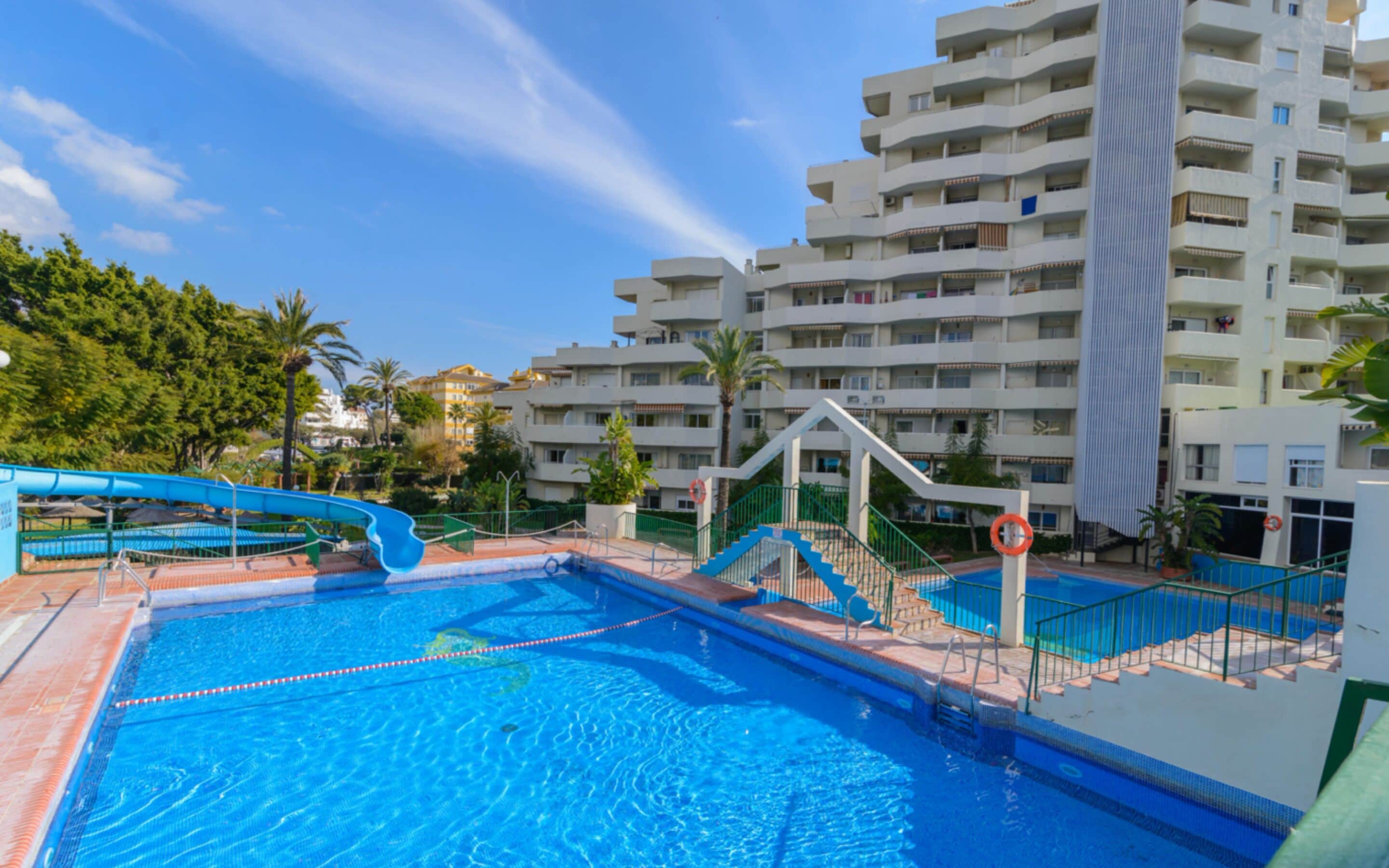 Una piscina con tobogán, rodeada por un edificio de varios pisos con balcones.