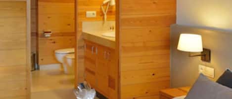 Een kamer met houten lambrisering, een bed, een nachtkastje, een lamp en een badkamer zichtbaar door een open deur.