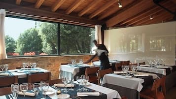 A restaurant with tables set for dining, large windows, and a wooden ceiling.