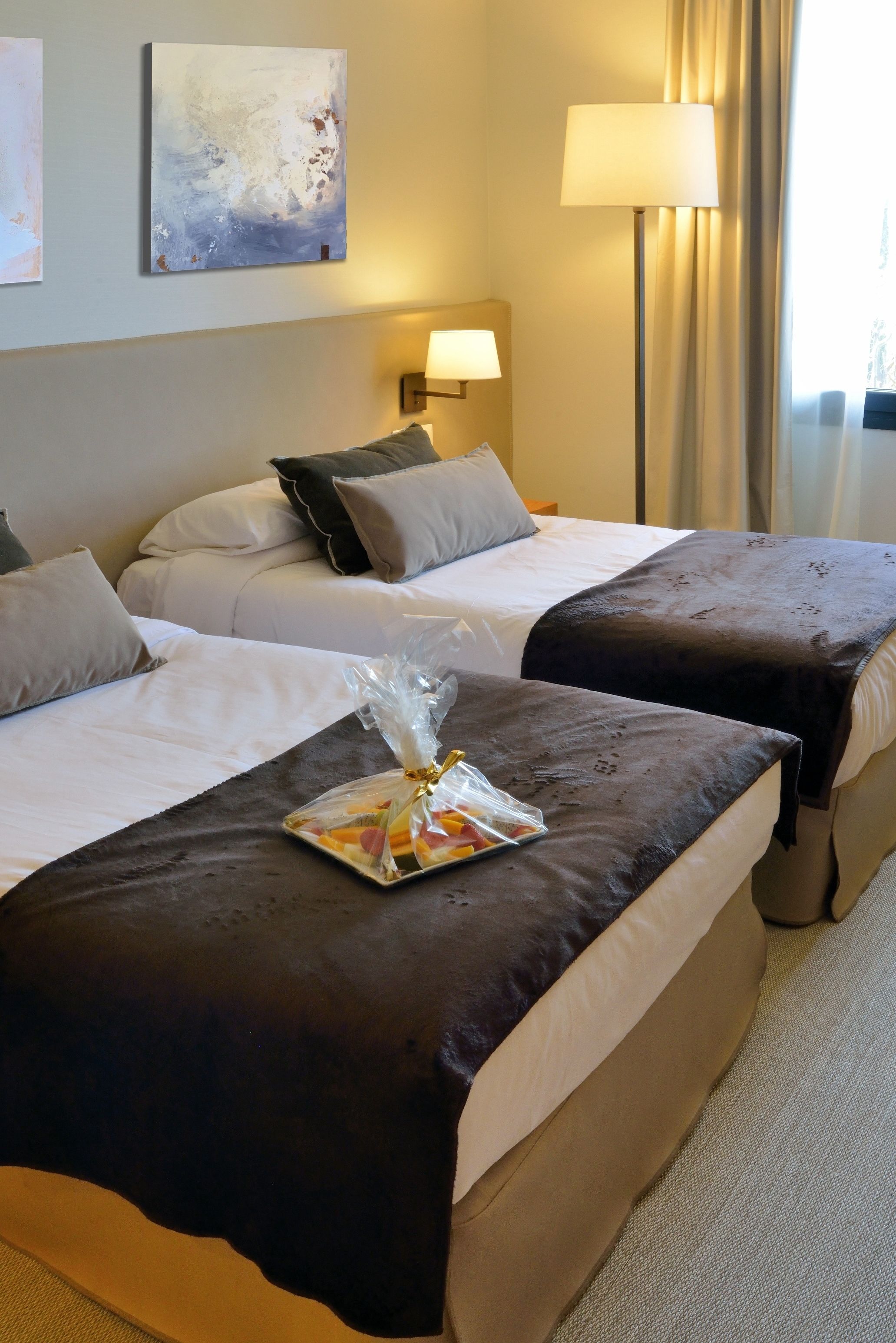 Quarto de hotel com duas camas, uma luminária, um quadro e uma bandeja com comida sobre a cama.