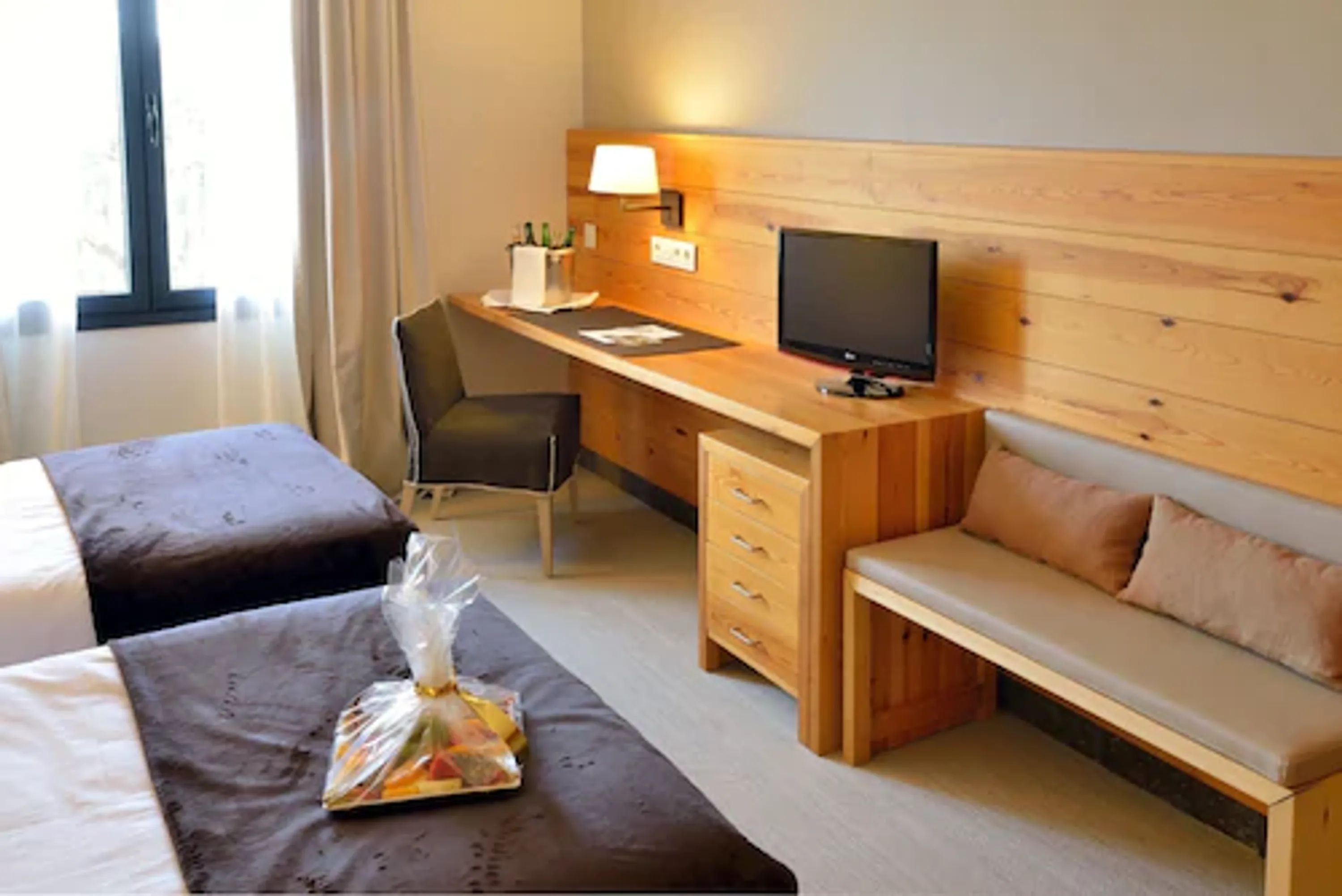 Habitación de hotel con dos camas, un escritorio con computadora y lámpara, un televisor y un área de descanso.