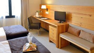 Habitación de hotel con dos camas, un escritorio con computadora y lámpara, un televisor y un área de descanso.
