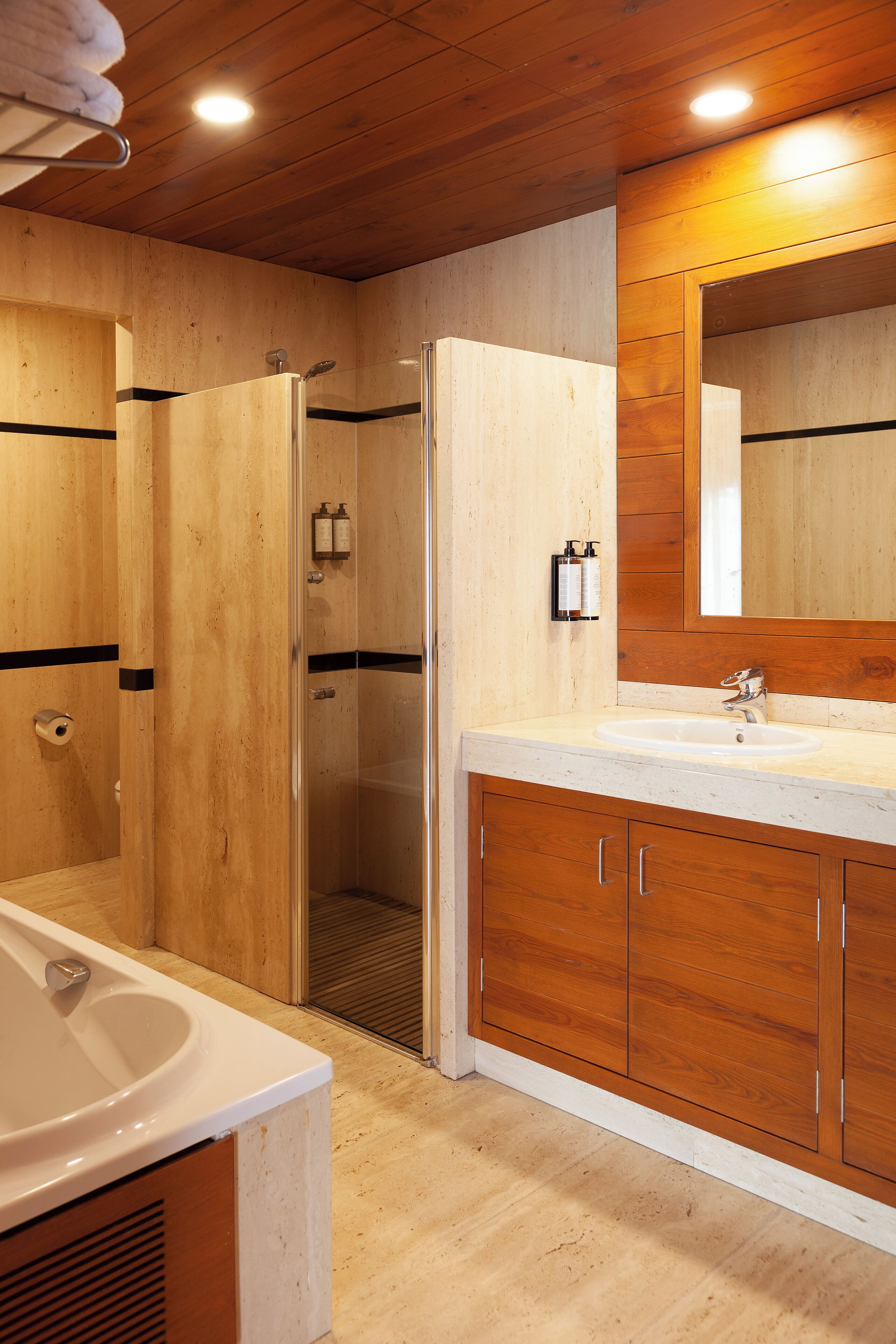 A wooden bathroom with a bathtub, a shower, and a vanity with a mirror.