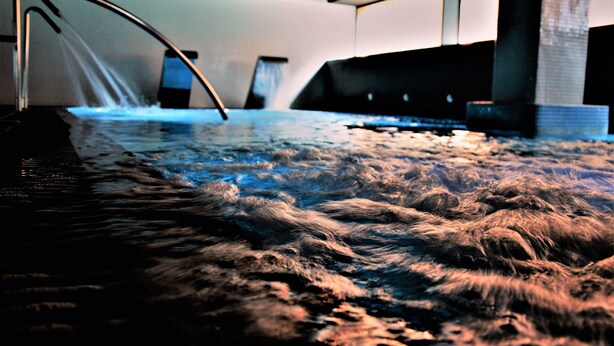 Una amplia piscina interior con un elemento acuático central y una estructura metálica curva.