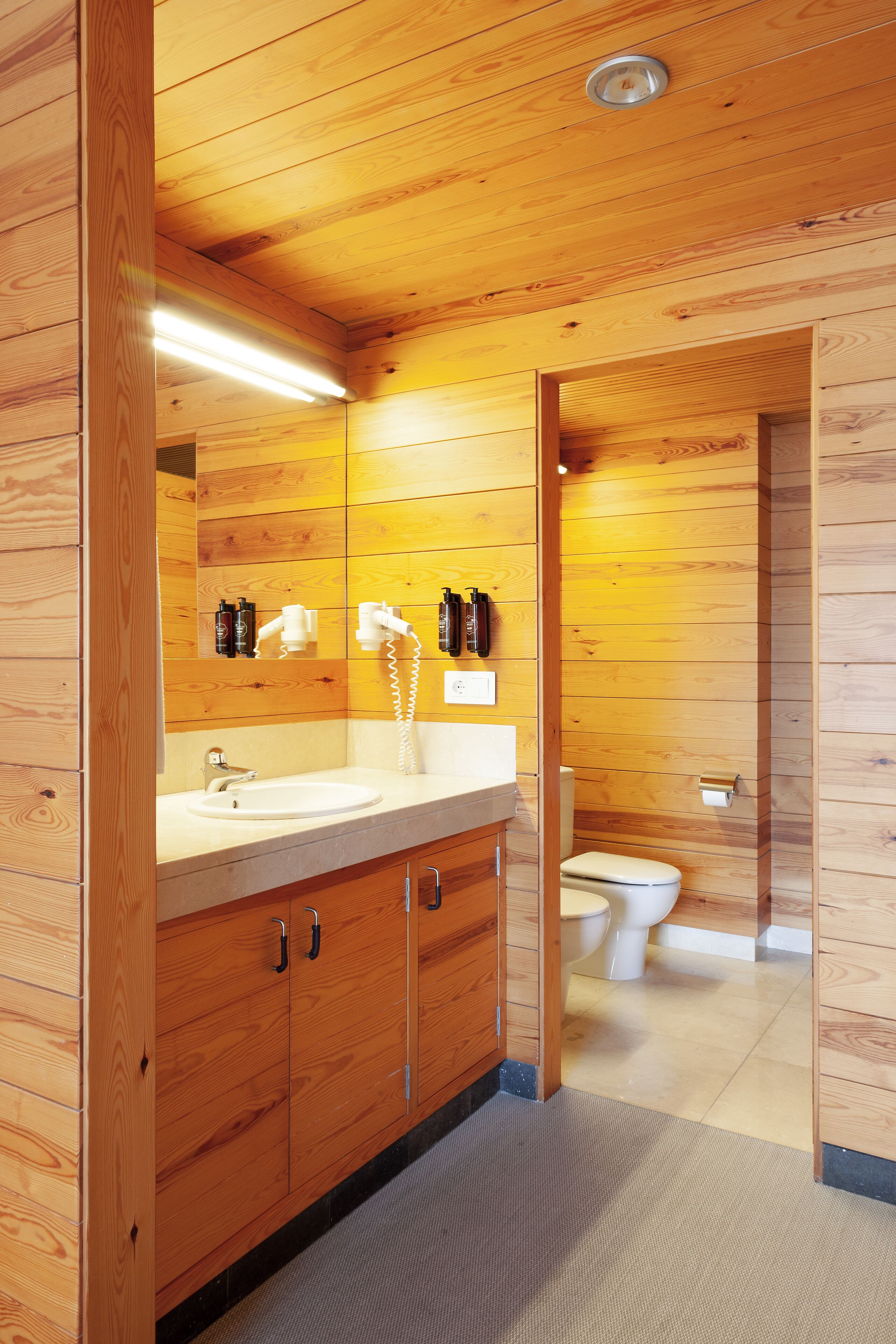 A wooden-paneled bathroom with a sink, mirror, and toilet.