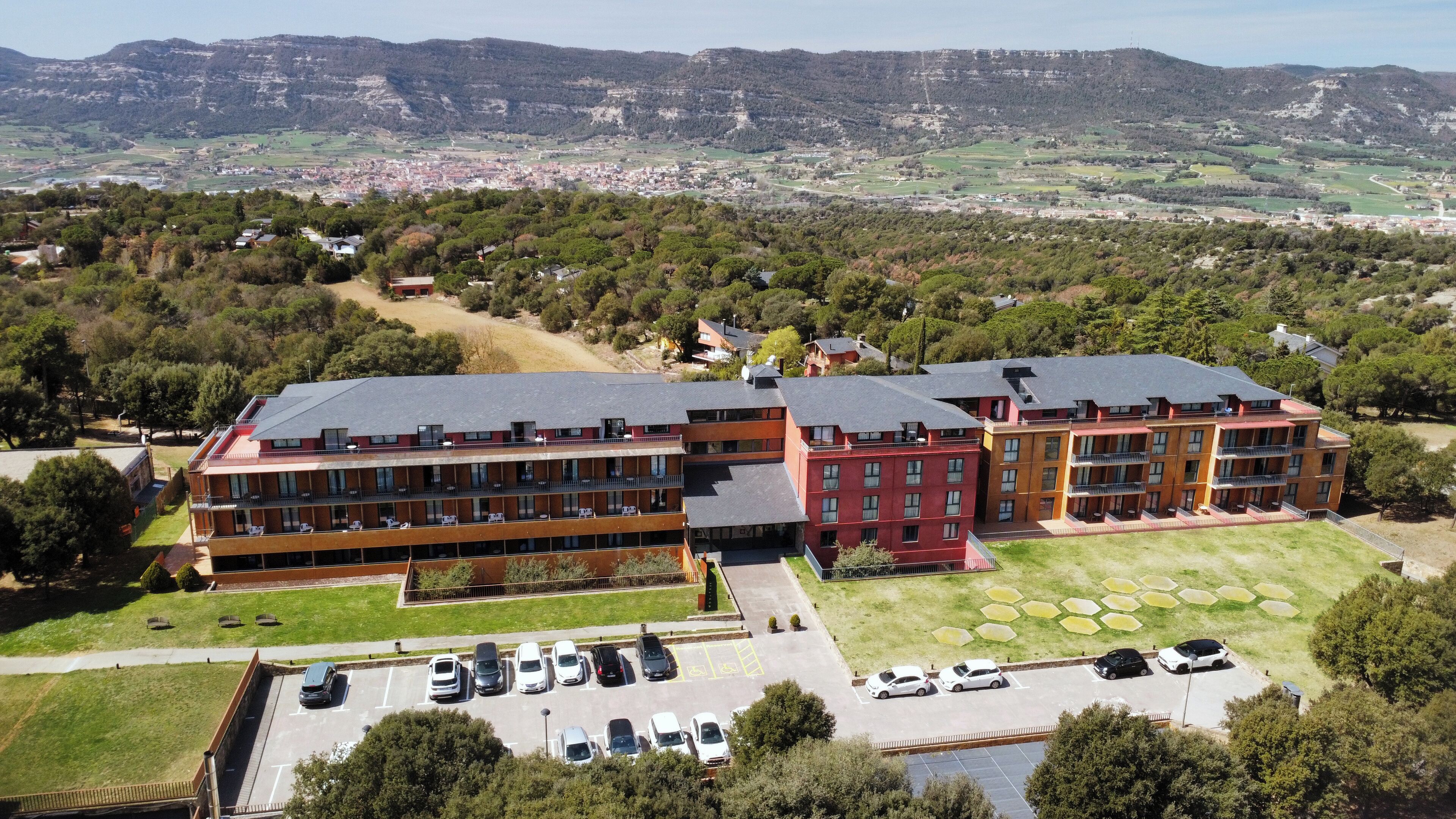 Un hotel de varios pisos con estacionamiento y vistas a un paisaje montañoso.