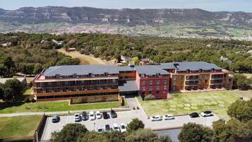 Un hotel de varios pisos con estacionamiento y vistas a un paisaje montañoso.