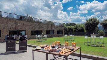 An outdoor buffet setup with a stone building in the background, a grassy area, and a clear sky.