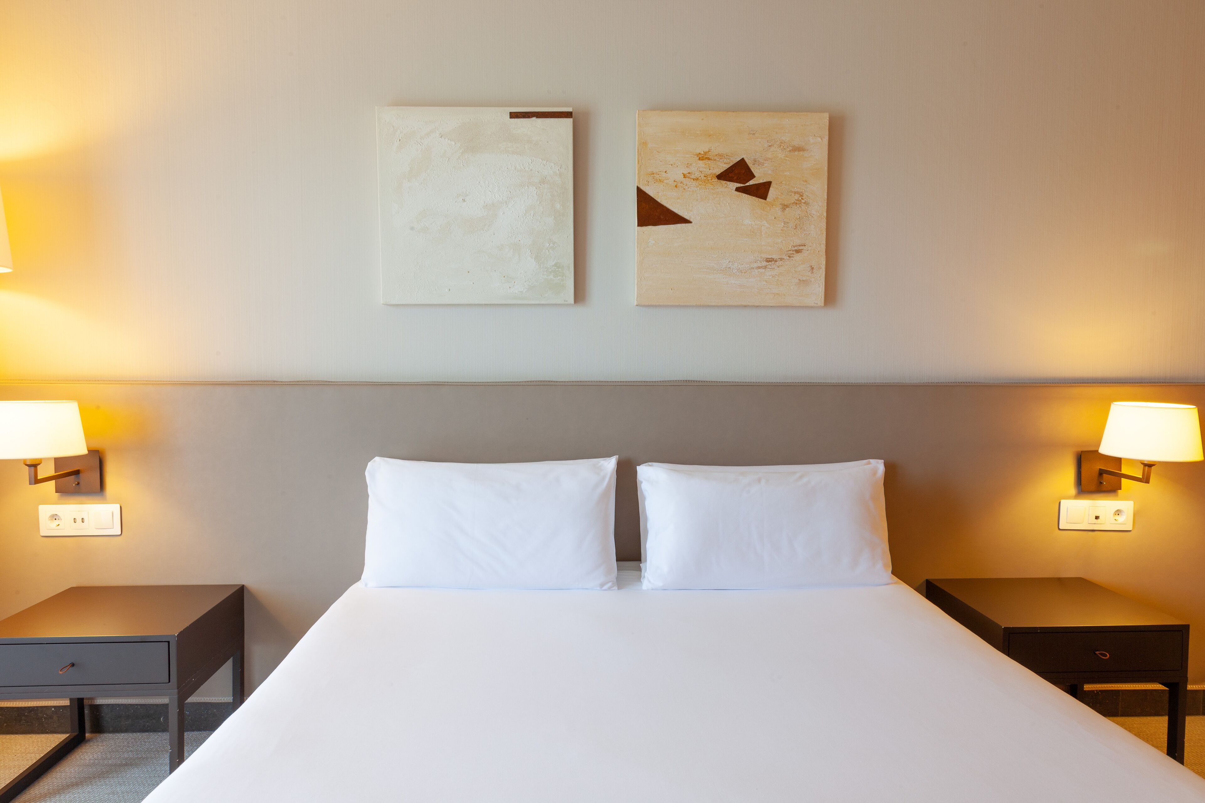 Een hotelkamer met een groot bed, twee nachtkastjes en twee wandlampen.