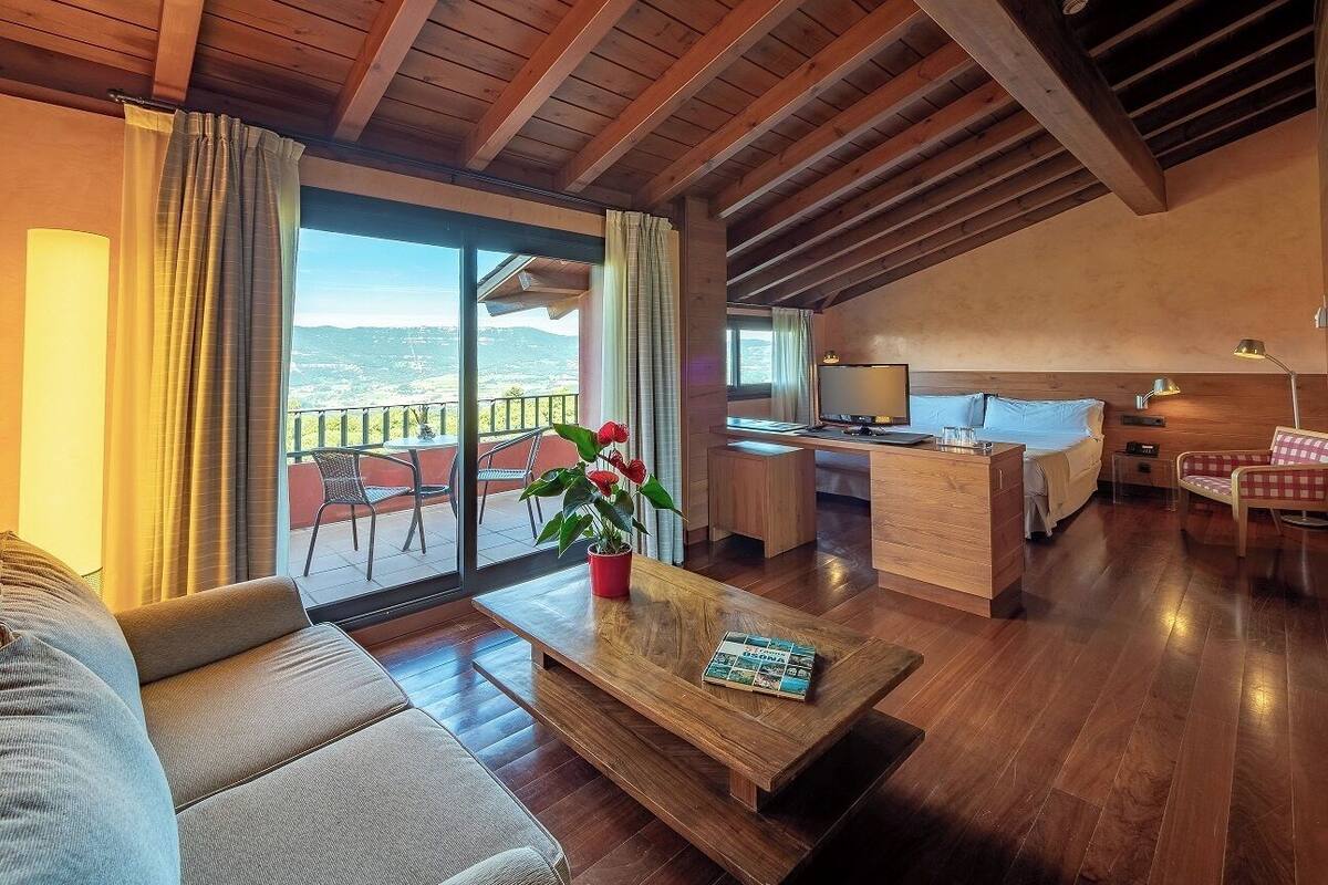 Amplia sala de estar con techo de madera, un sofá, una mesa de centro con una revista y vistas a un balcón con mesa y sillas.