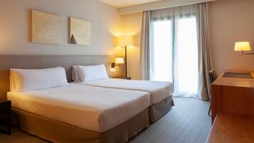 A hotel room with two beds, a desk, and a lamp.