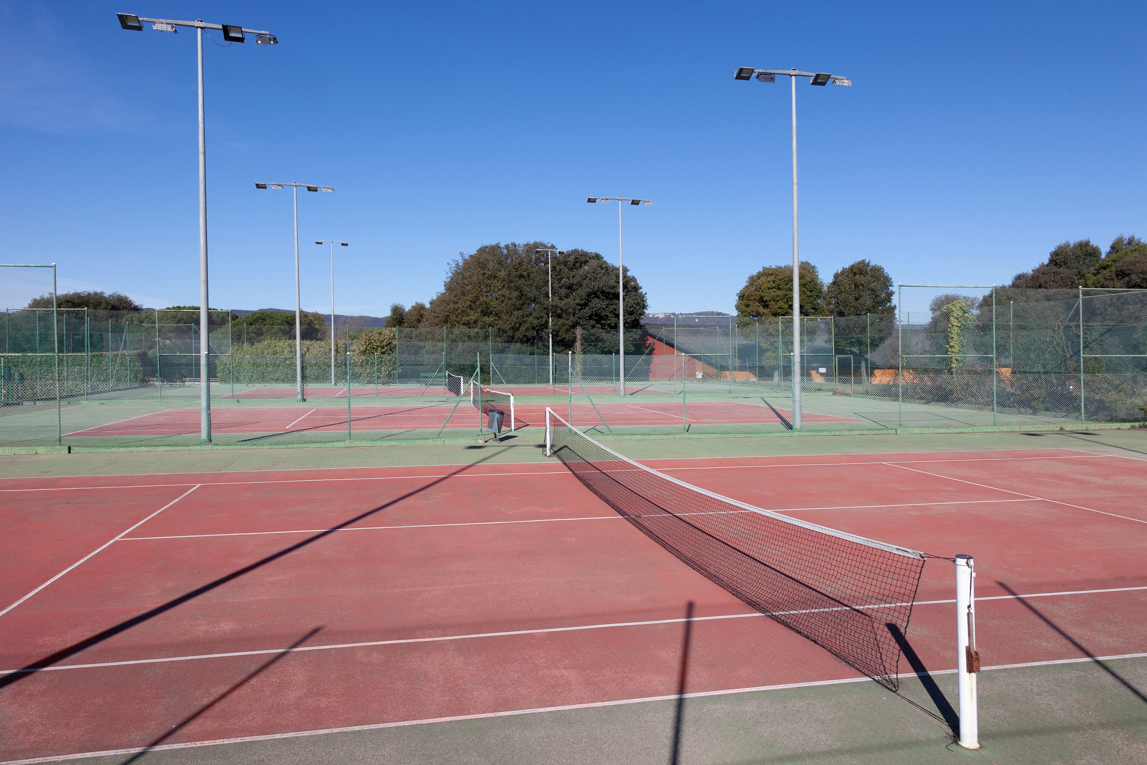 A tennis court with multiple light poles, a net, and a fence.