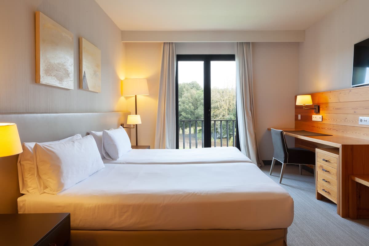 Habitación de hotel con dos camas, un escritorio, una silla y un televisor.