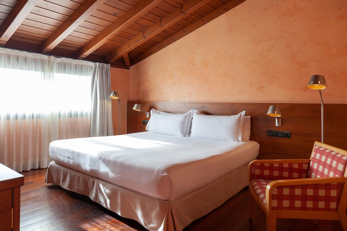 Una cama bien tendida con sábanas blancas, techo de madera y dos lámparas de noche.