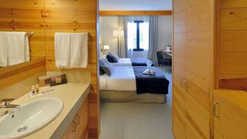 Habitación de hotel con interior de madera, una cama grande, un escritorio y un baño con lavamanos y espejo.