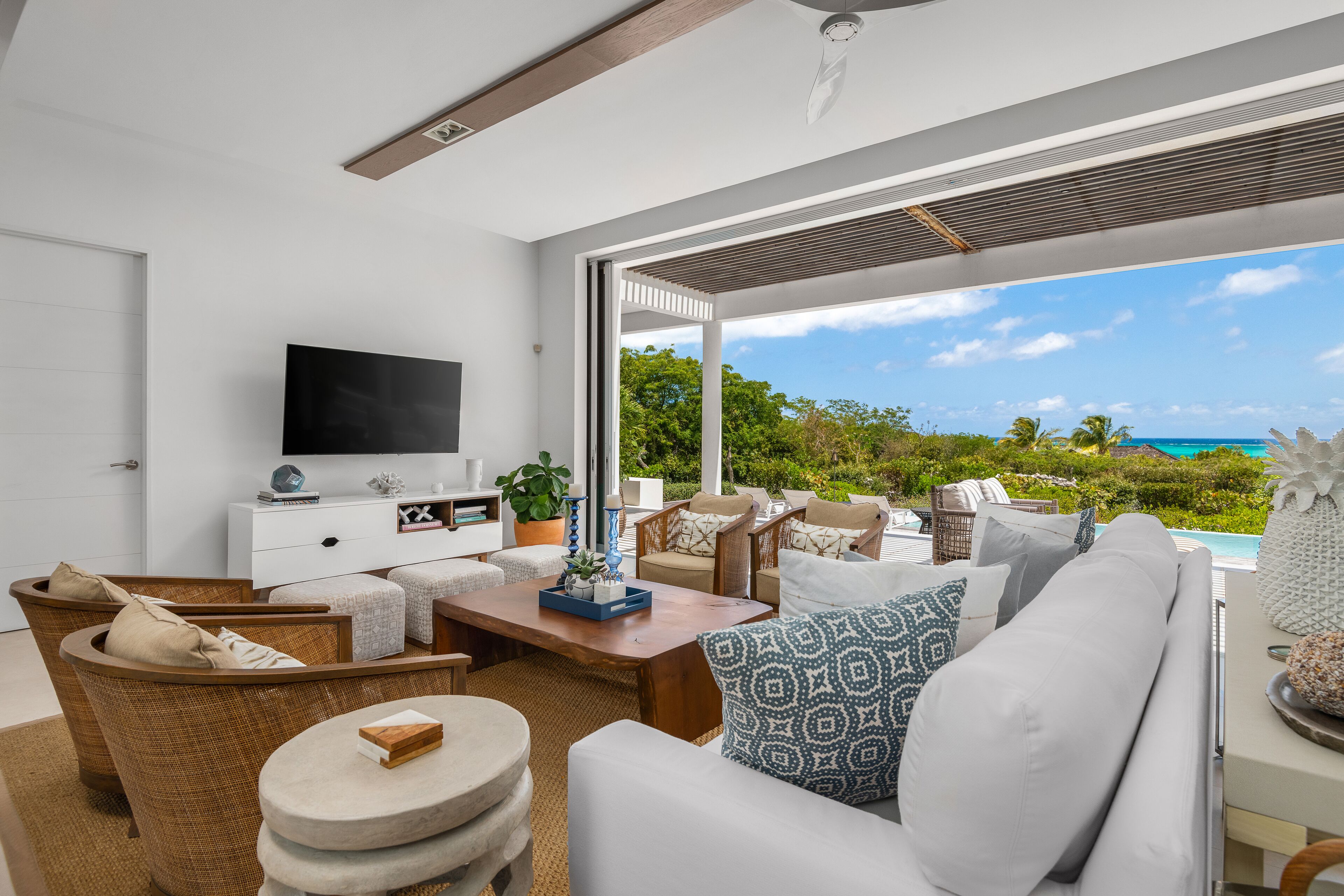 A modern living room with a large TV, comfortable seating, a coffee table, and a view of the ocean.