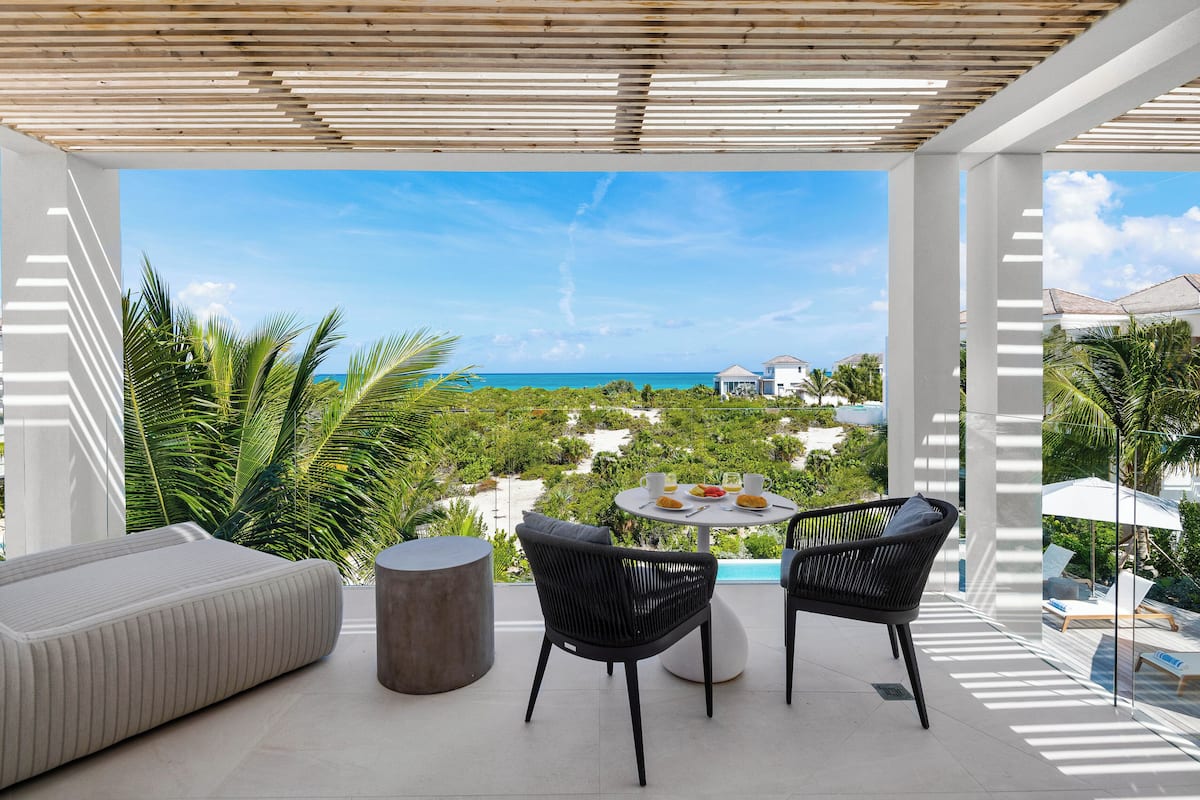 A balcony with a view of the ocean, a round table with chairs, and a cushioned seating area.
