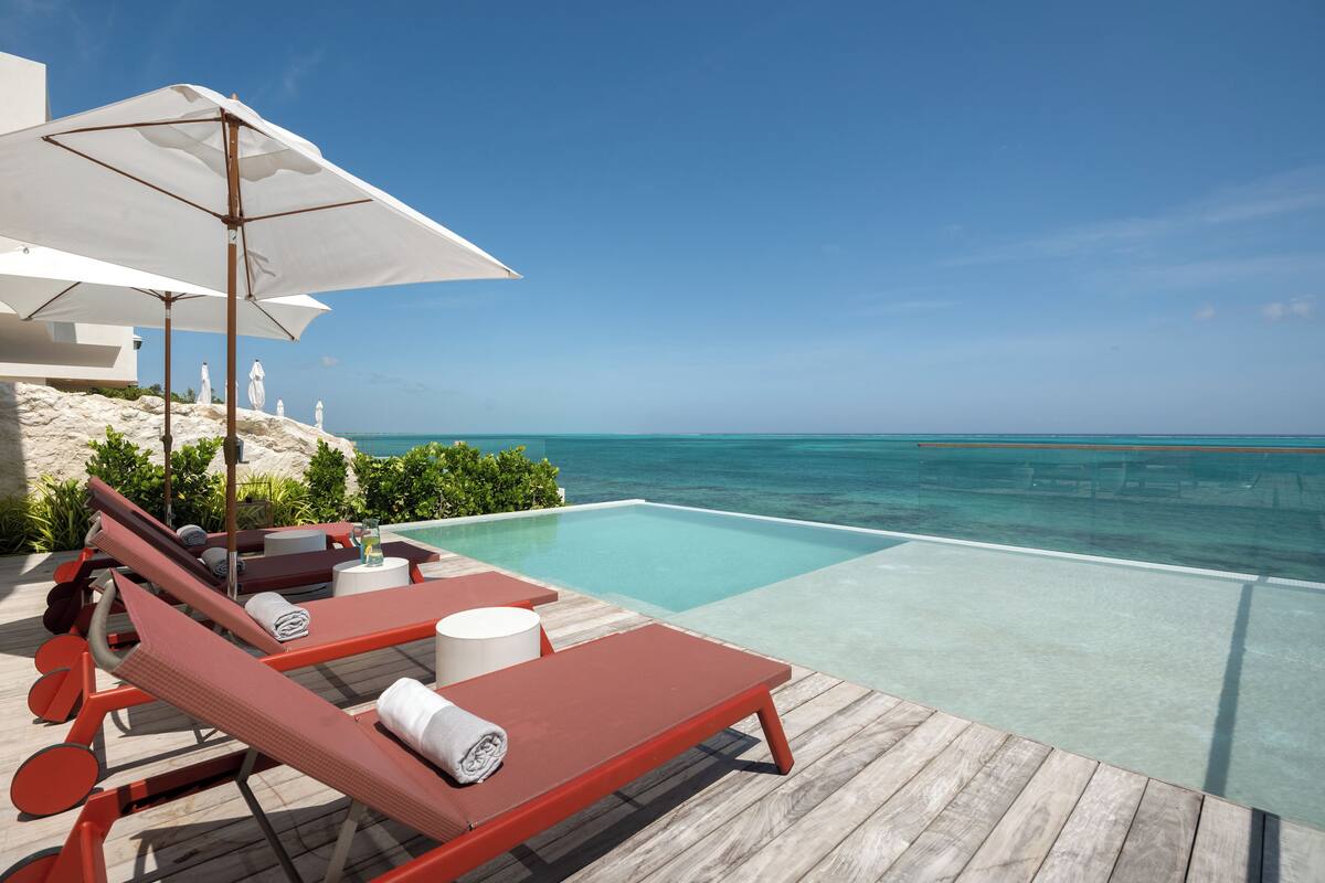 A poolside area with lounge chairs and umbrellas, overlooking a clear blue sea.