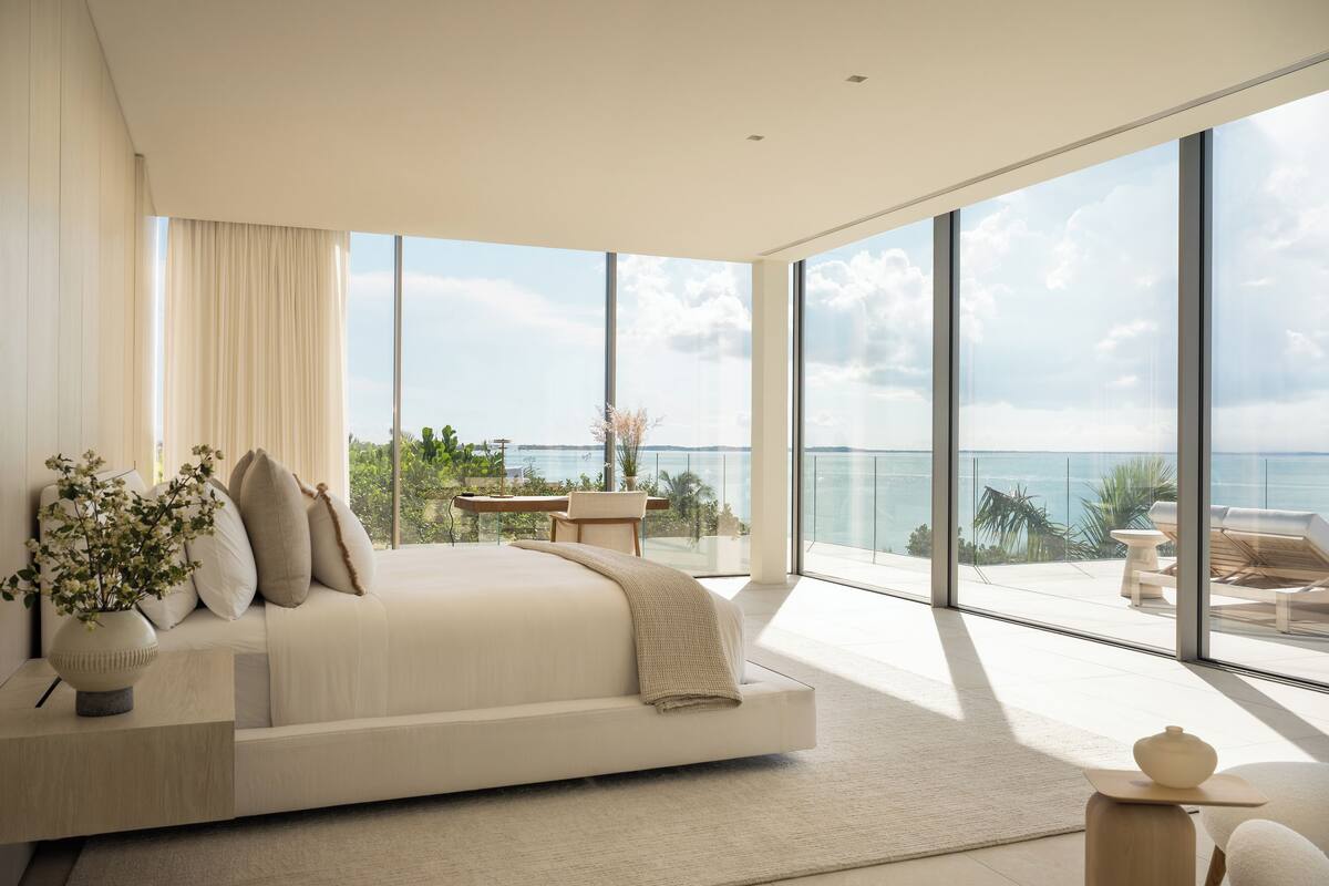 A modern bedroom with a large bed, a view of the ocean, and a balcony with outdoor furniture.