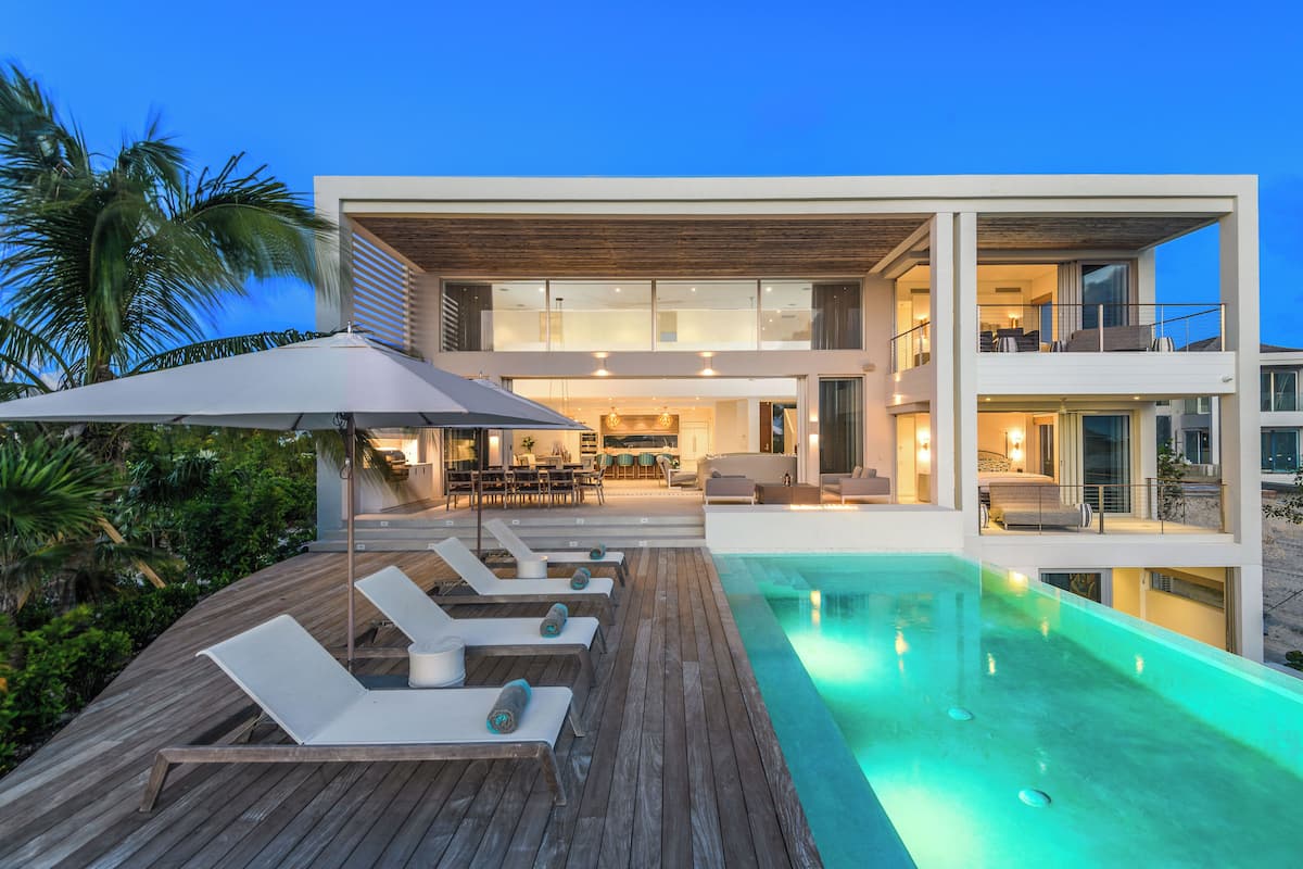 A modern two-story house with a swimming pool, outdoor seating, and a balcony.