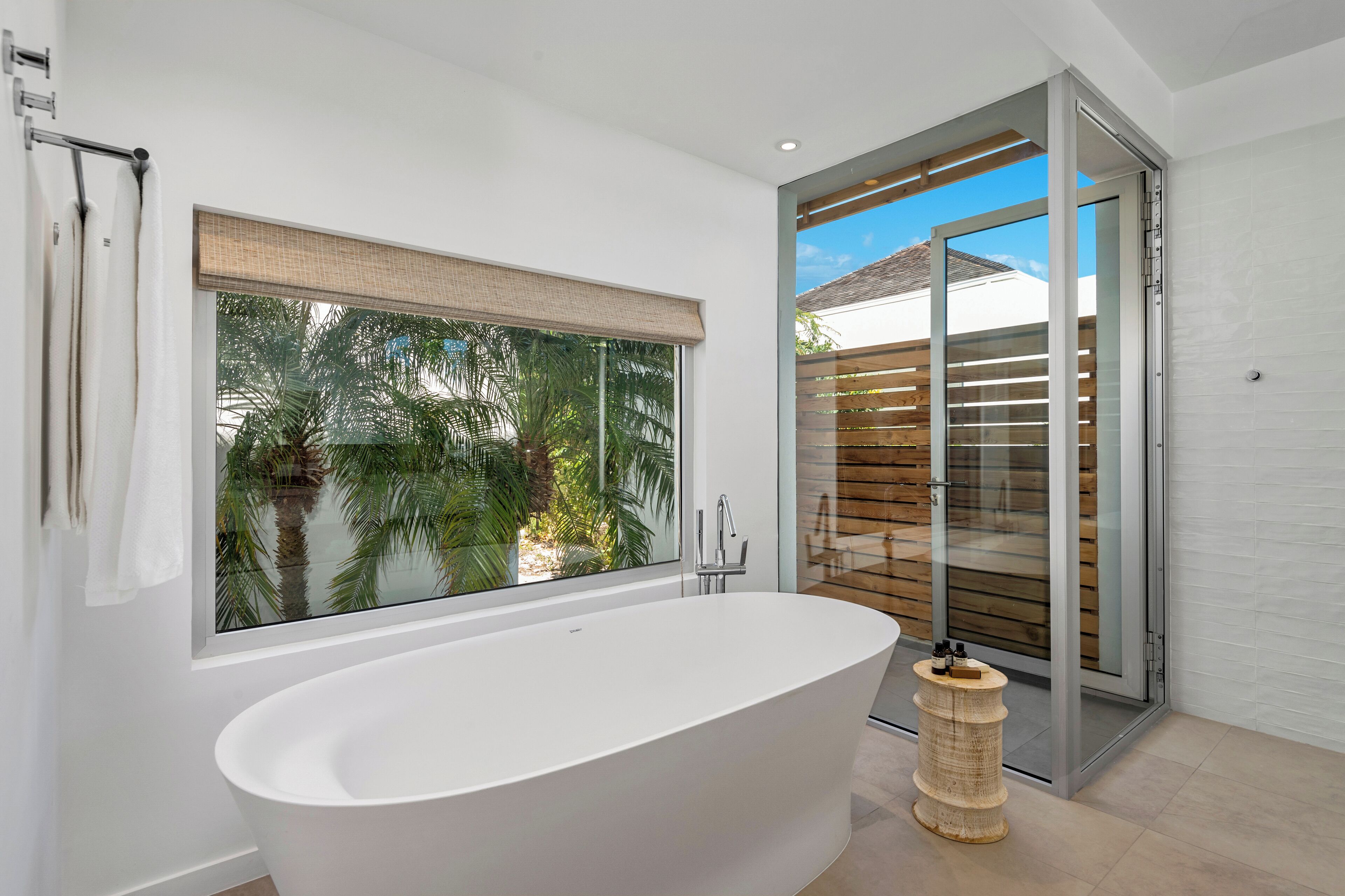 Ein modernes Badezimmer mit freistehender Badewanne, einem großen Fenster mit Blick auf Palmen und einer Schiebetür zu einem Außenbereich.