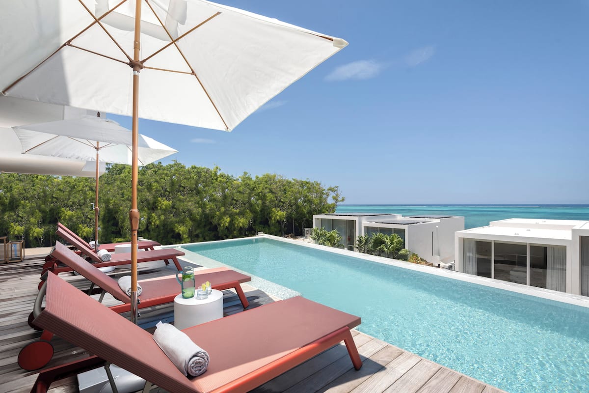 A poolside area with lounge chairs and umbrellas, a clear view of the ocean, and a wooden deck.