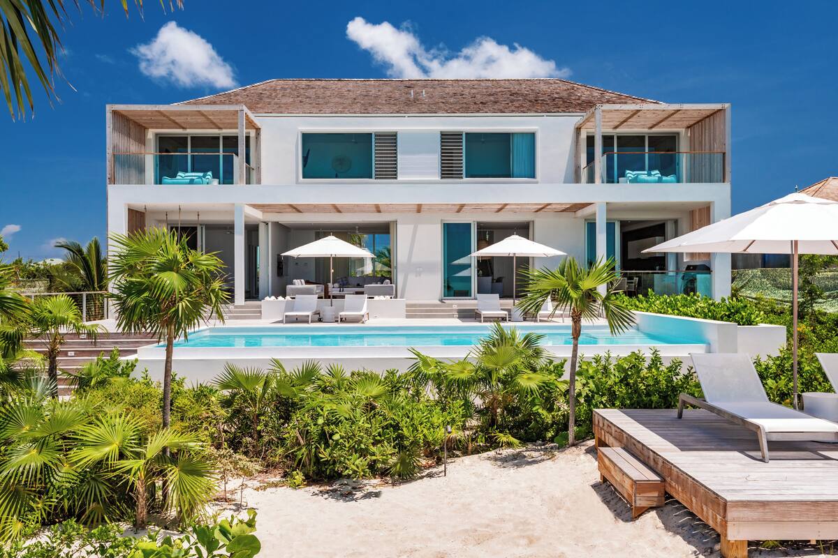 A modern two-story house with a swimming pool, outdoor seating, and lush greenery.