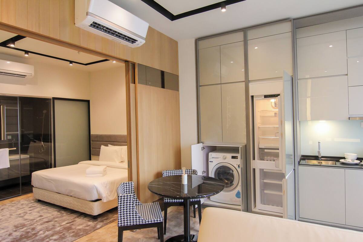 A hotel room with a bed, a table with chairs, a washing machine, and a kitchenette.