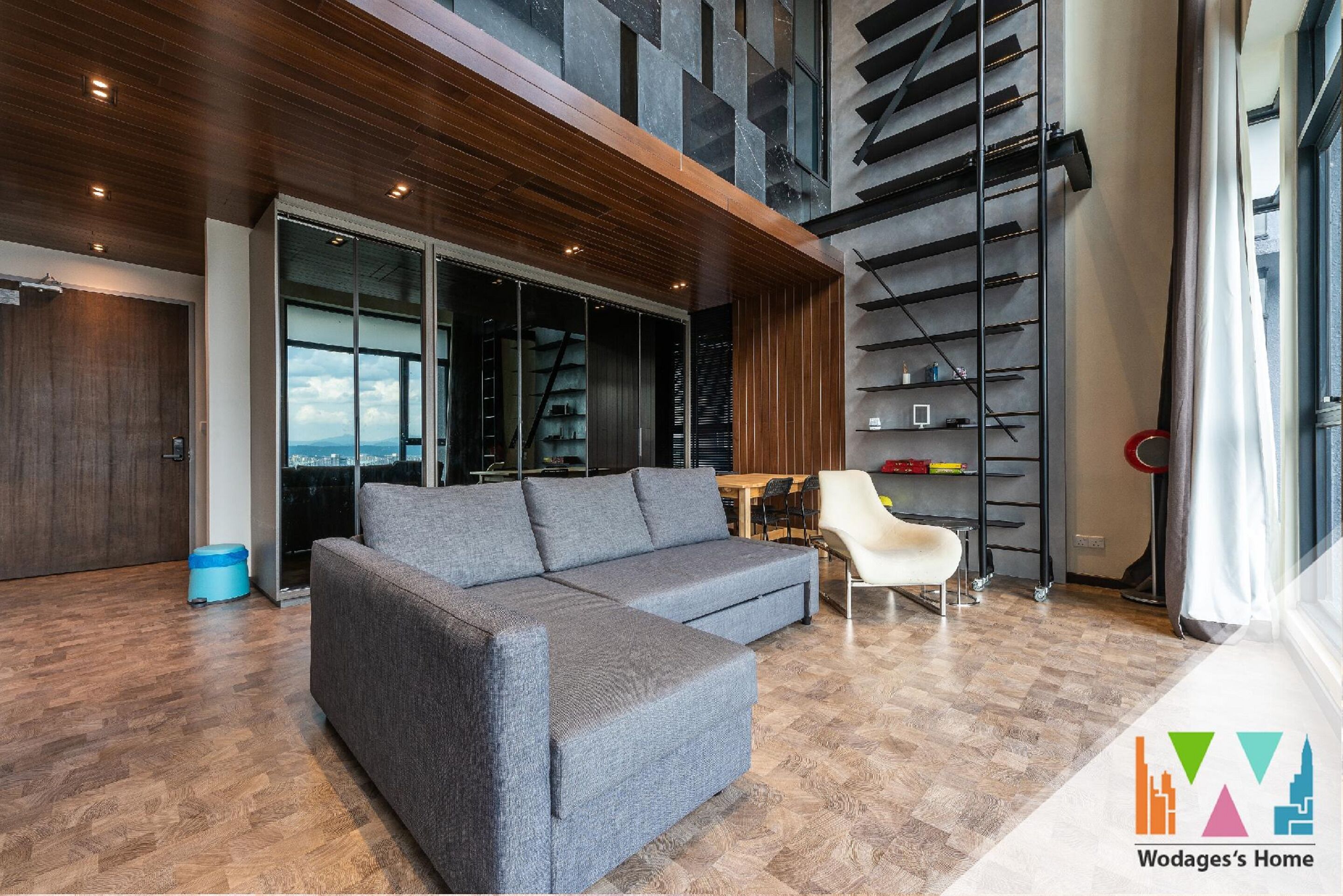 A modern living room with a sectional sofa, a dining area, and a staircase leading to an upper level.