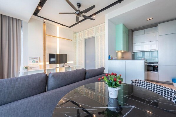 Una sala de estar moderna con un sofá gris, una mesa redonda de vidrio y un ventilador de techo.