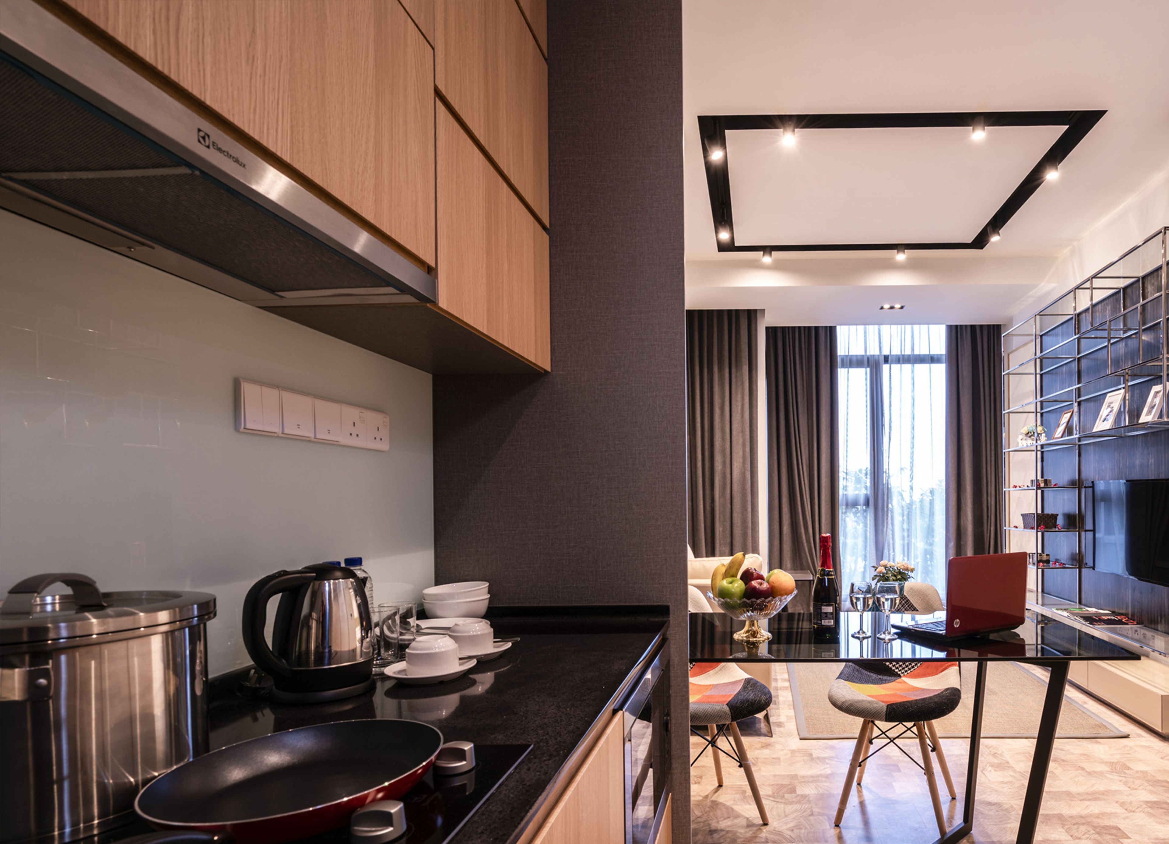 Una cocina moderna con electrodomésticos de acero inoxidable, un comedor con mesa de vidrio y un espacio de estar con una estantería y televisor.