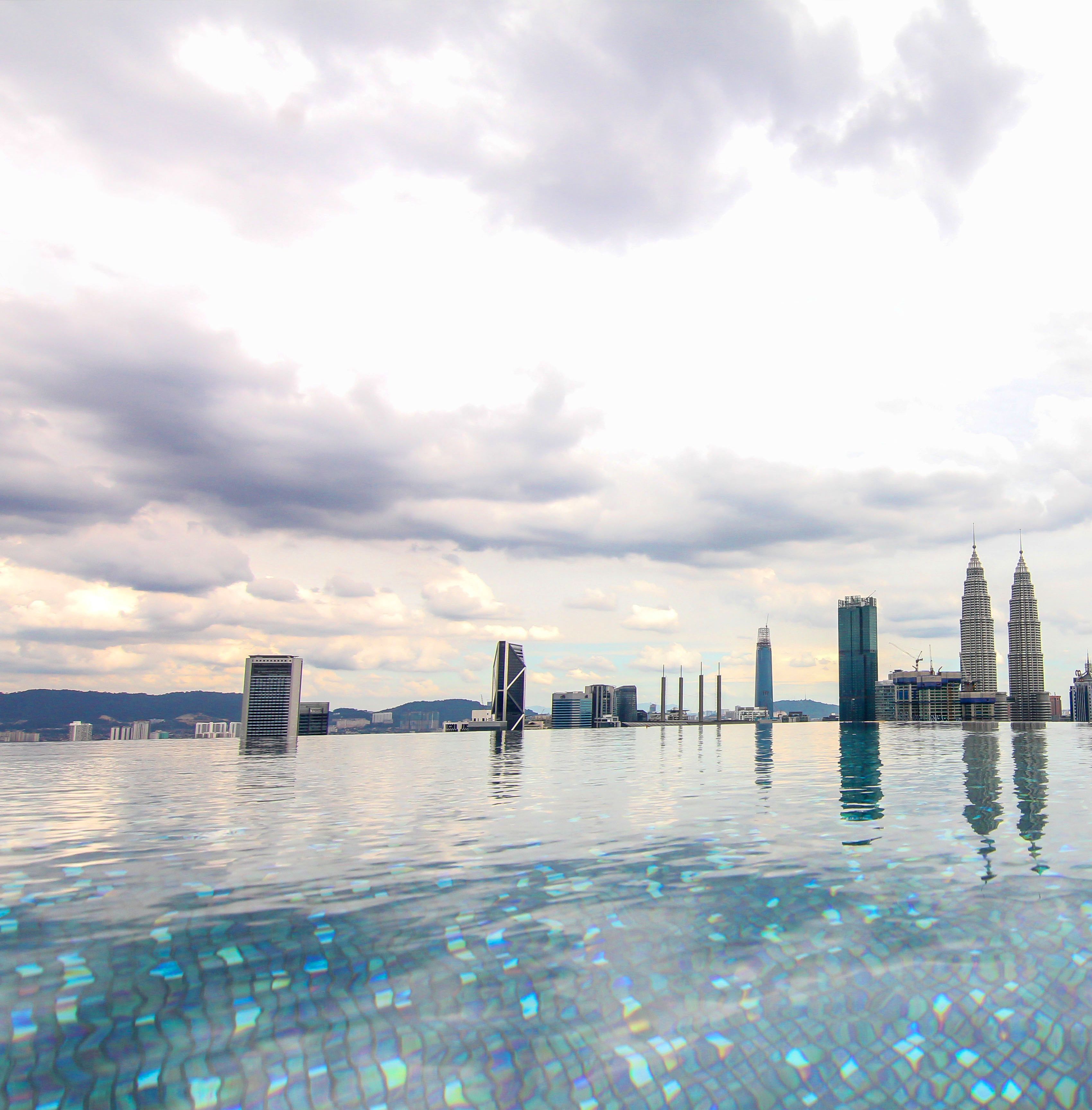 A city skyline reflected in calm water, with prominent buildings including the Petronas Towers.