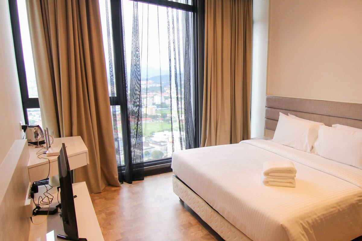 A hotel room with a bed, a desk with a computer, and a window with curtains.