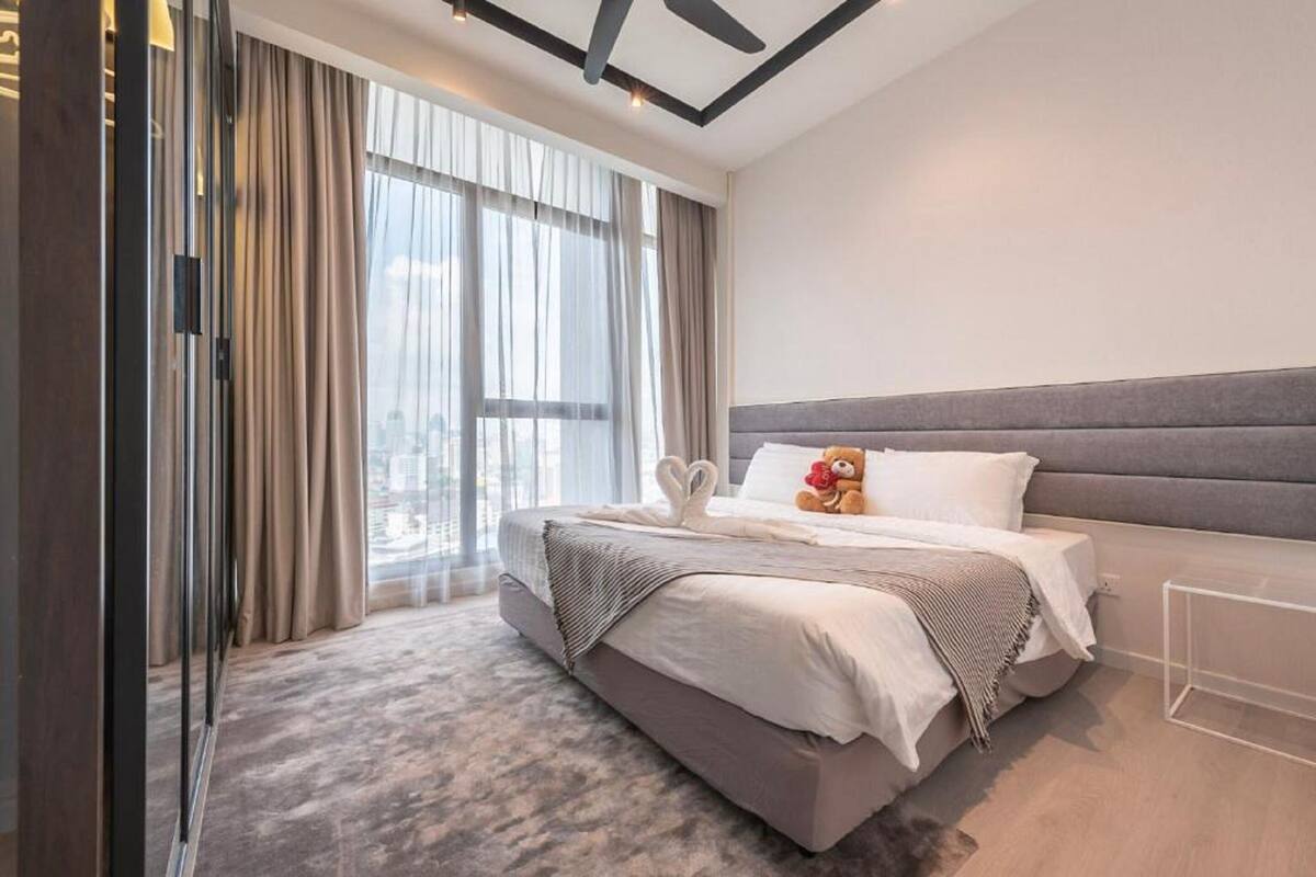 A modern hotel room with a large bed, a city view, and a glass door leading to a balcony.