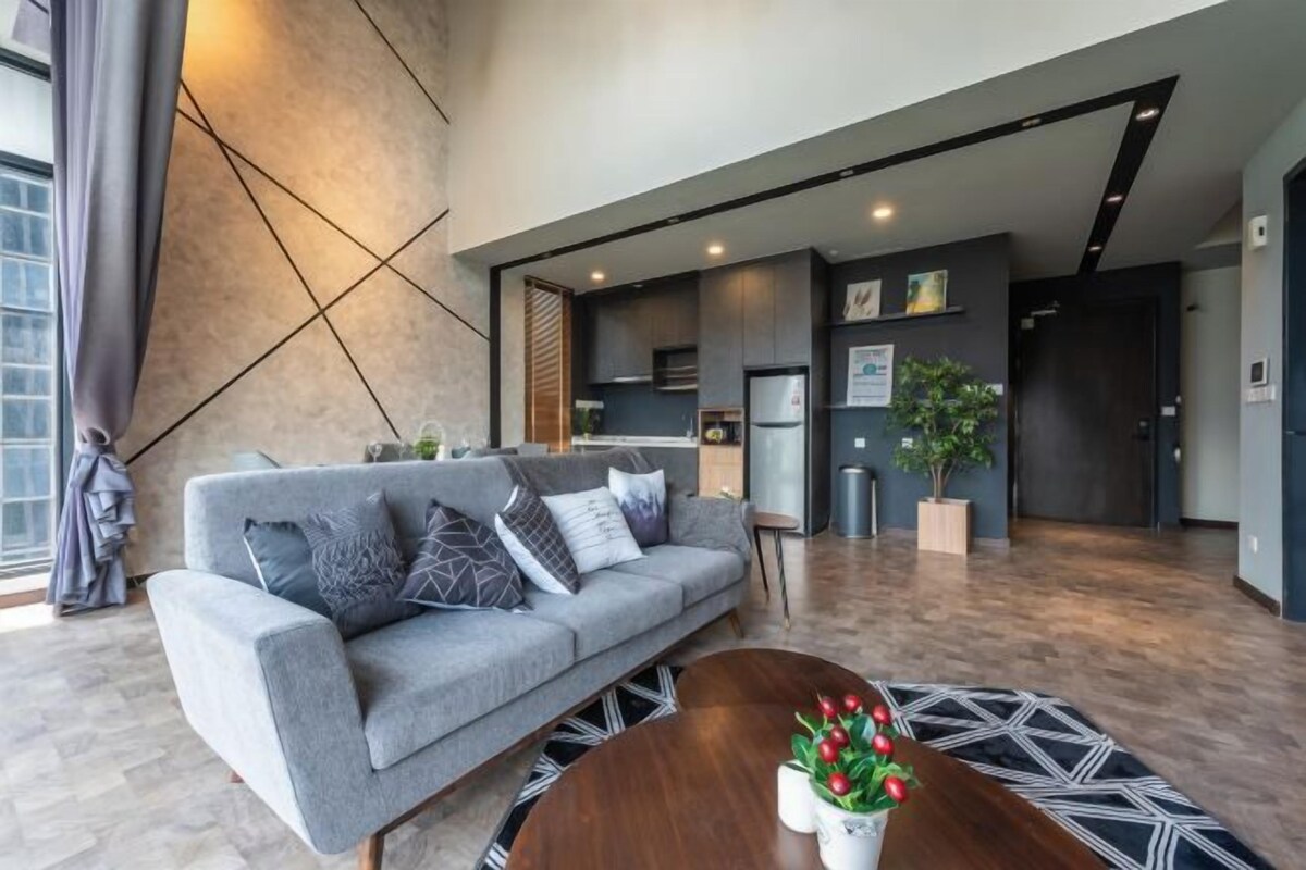 A modern living room with a grey sofa, a round coffee table with a vase, and a kitchen in the background.