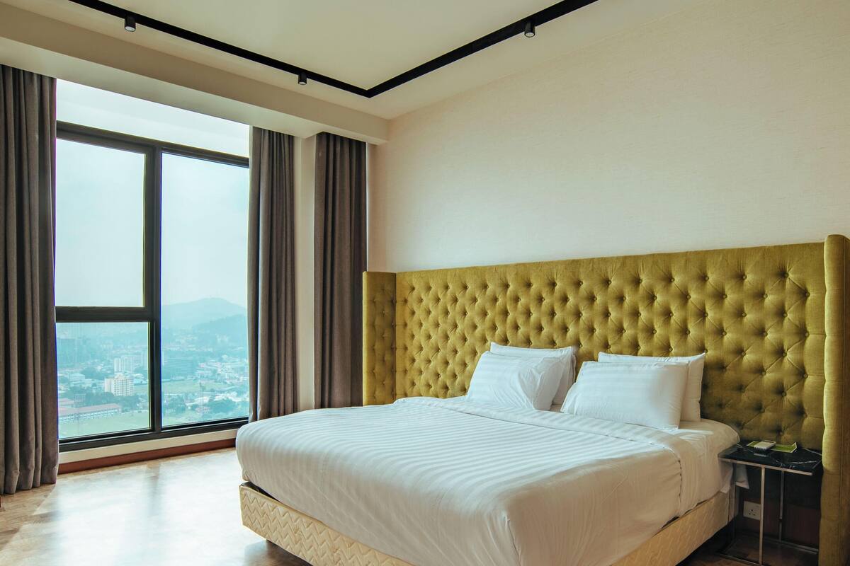 A hotel room with a large bed, a nightstand, and a view of a cityscape through a large window.