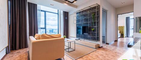 A modern living room with a sofa, a TV mounted on a wall, and a large window offering a city view.