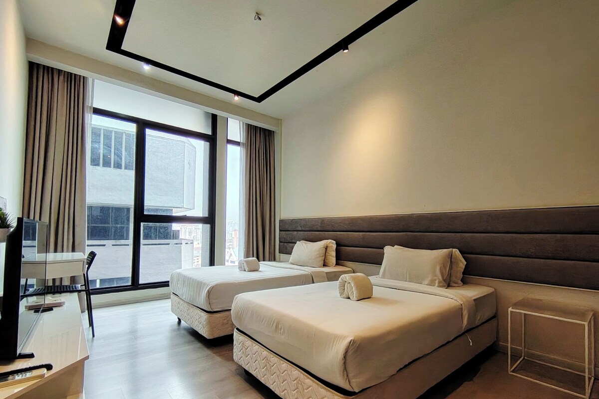 A hotel room with two beds, a desk, and a large window.