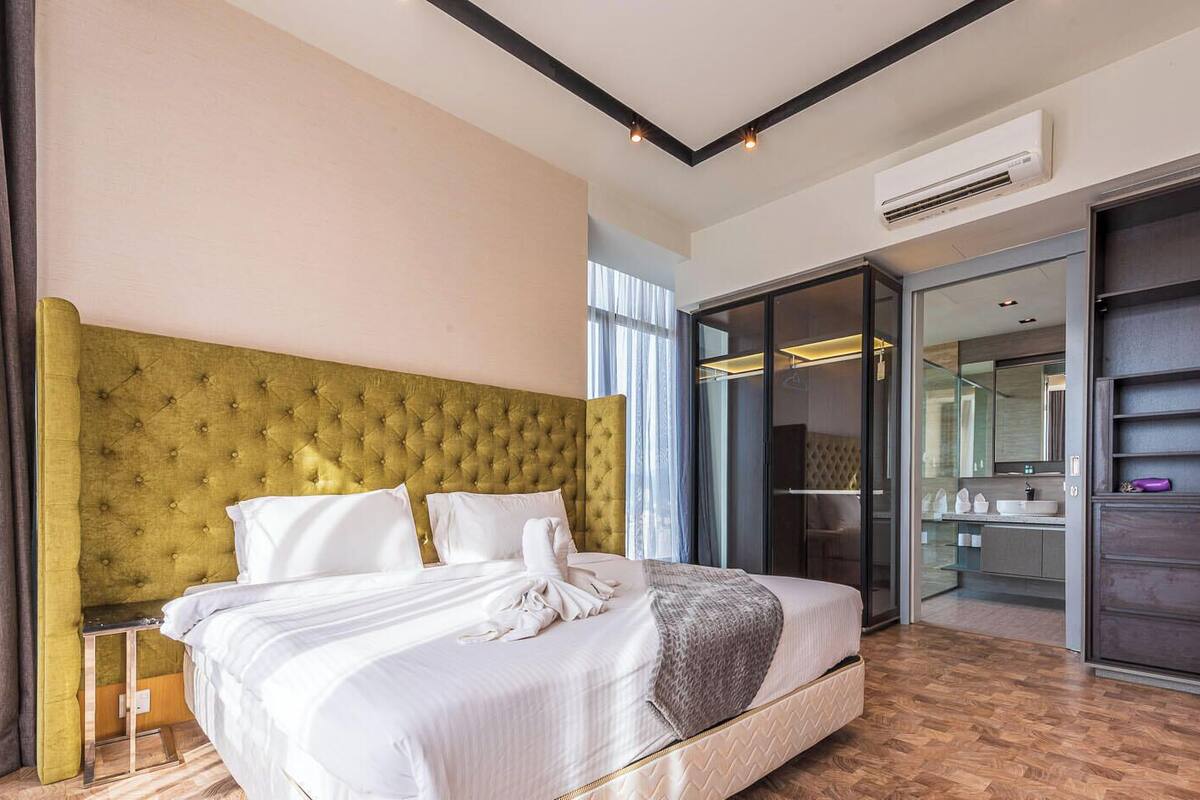 A modern hotel room with a large bed, a headboard, an air conditioning unit, and a sliding door leading to a bathroom.