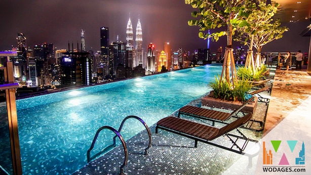 Ein Poolbereich bei Nacht mit Liegestühlen und Blick auf die Skyline der Stadt, darunter die Petronas Towers.