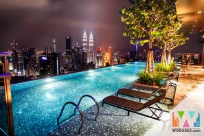 A nighttime pool area with lounge chairs and a view of the city skyline, including the Petronas Towers.