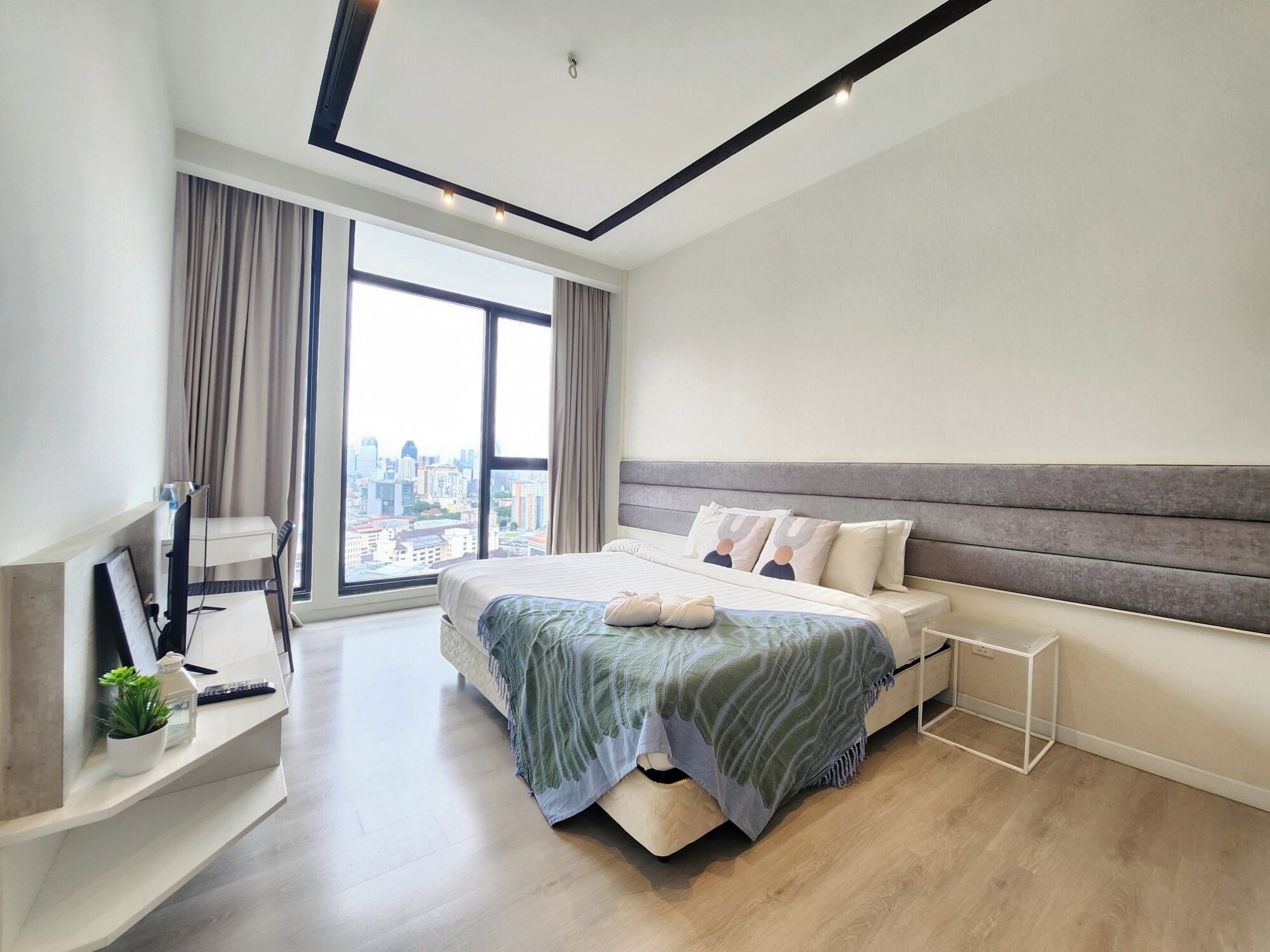 A modern bedroom with a large bed, a desk, and a view of a cityscape.