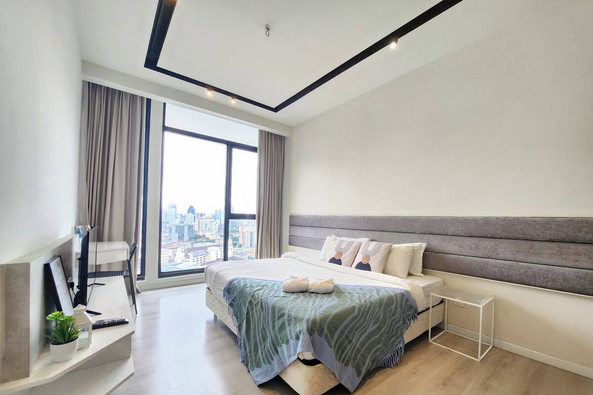 A modern bedroom with a large bed, a desk, and a view of a cityscape.