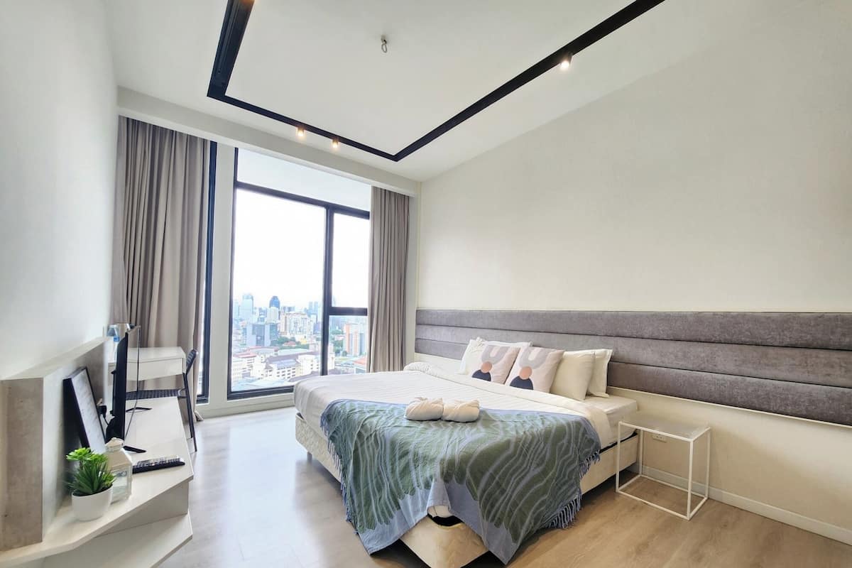 Ein modernes Schlafzimmer mit einem großen Bett, einem Schreibtisch und Blick auf eine Stadtlandschaft.